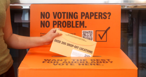 Person placing an official orange voting envelope into a ballot box.