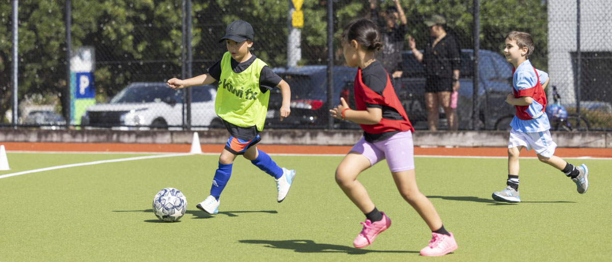 Three young children playing football on an outdoor pitch. 