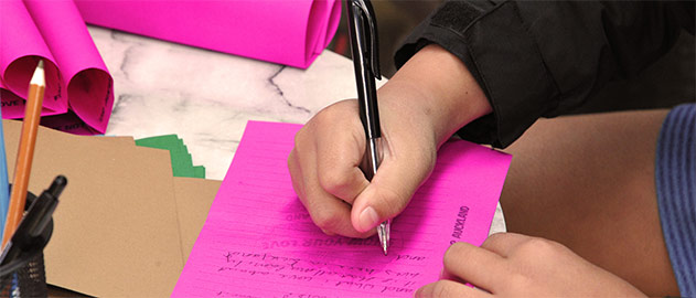 Close up of a hand writing on a pink form. 